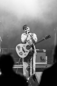 Xesse in bianco e nero mentre canta sul palco con la chitarra